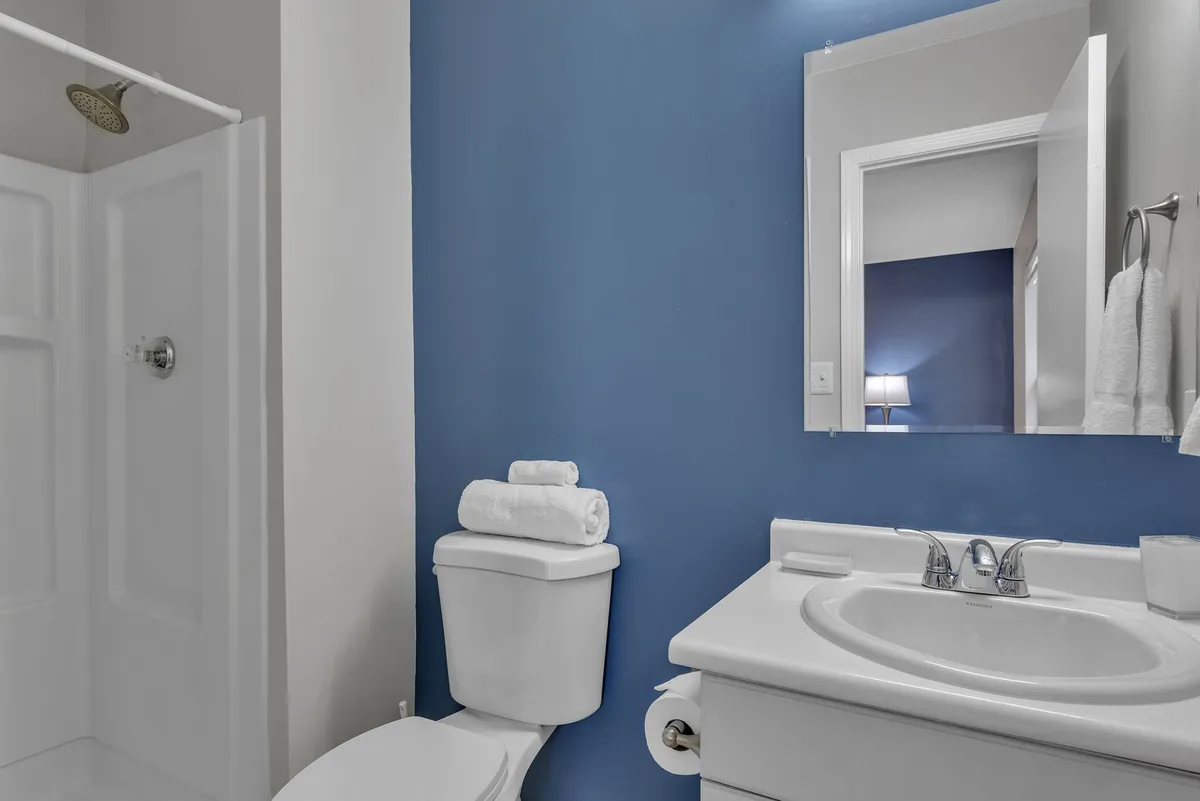 A contemporary bathroom space featuring a soothing blue wall, a sleek sink, toilet, mirror, and a modern shower area. The mood is inviting and clean, ideal for both quick morning routines and quiet moments of self-care.