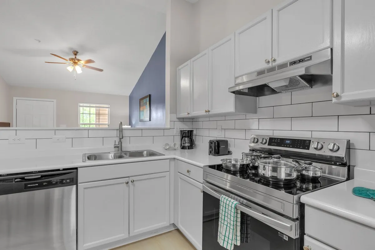 A spacious modern kitchen featuring stainless steel appliances, white cabinetry, and a contemporary backsplash. The kitchen is equipped with a full-size refrigerator, oven, microwave, and generous counter space, all bathed in welcoming natural light.