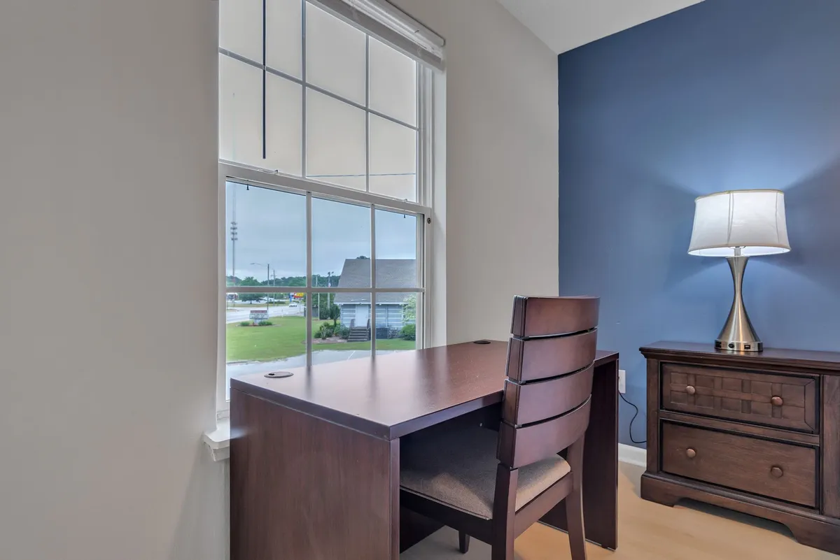 Inside, the image features a dedicated workspace with a desk, lamp, and window, capturing a tranquil and focused mood. The setup is ideal for remote work or business tasks, offering natural light and a comfortable environment for productivity.
