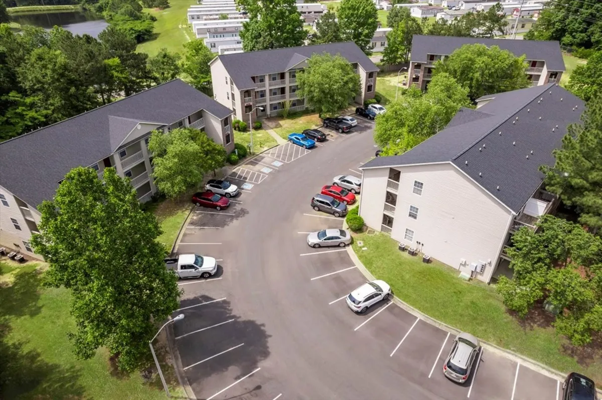 This photo captures the friendly, welcoming exterior of the apartment buildings, with green trees providing a natural backdrop. Residents can be imagined walking along the pathways or socializing in the communal areas, emphasizing the sense of community. The parking lot and open spaces suggest convenience for those returning from outdoor adventures.