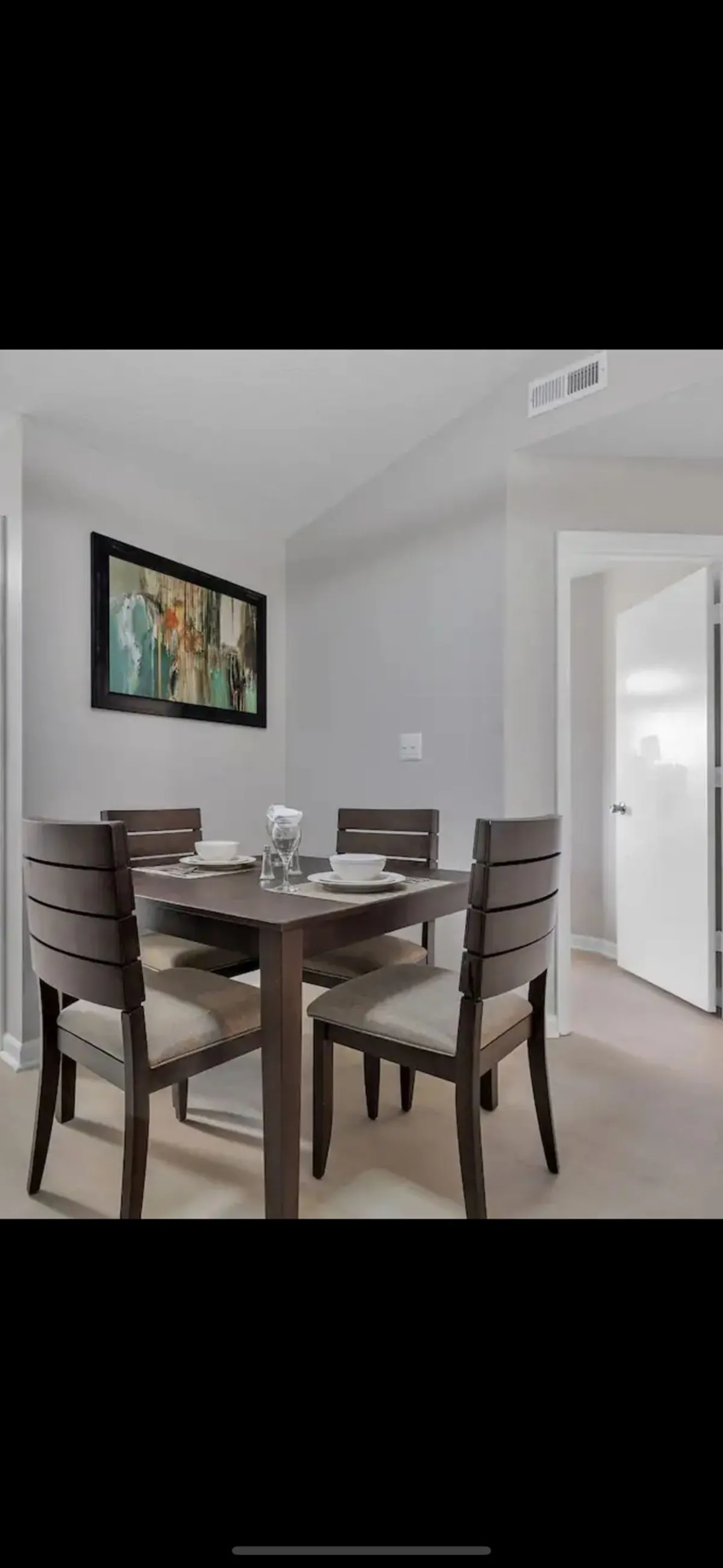 A warm interior scene centered around a dining table and chairs, with inviting artwork on the wall. While the main focus is on the dining area, the background hints at adjacent spaces, potentially alluding to seamless flow and ample storage.