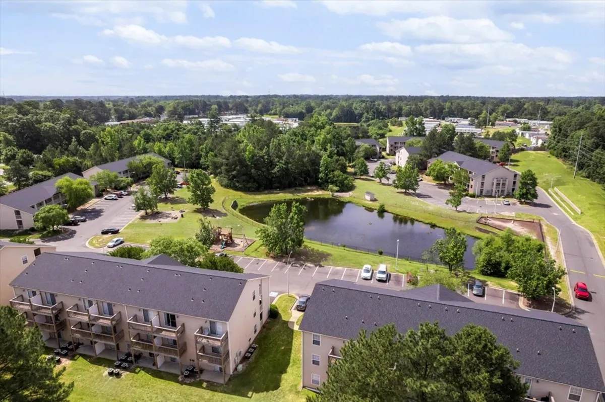 An inviting pond surrounded by lush greenery and nearby residential buildings, with space for family gatherings and outdoor recreational activities. The tranquil view highlights walking paths and open green space perfect for group outings and relaxation.