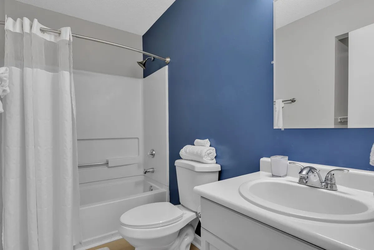 A bright bathroom with a calming blue accent wall, a pristine white bathtub, and a well-appointed sink area with toiletries. The space feels serene and welcoming, perfect for unwinding after a long day.