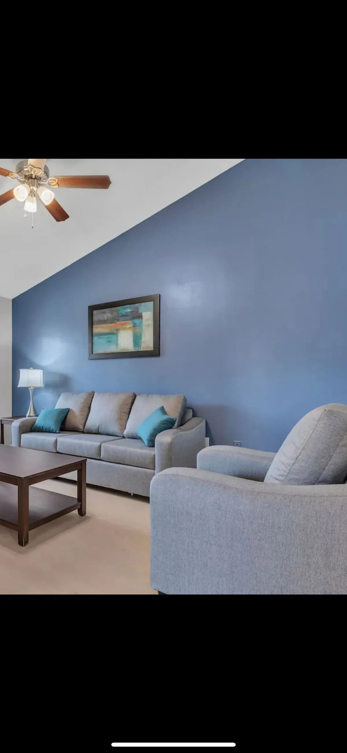 A bright, inviting living room with a comfortable sofa set against a striking blue wall, complemented by modern artwork and a stylish coffee table. Warm lighting from a standing lamp enhances the cozy atmosphere, making it perfect for relaxing or socializing.
