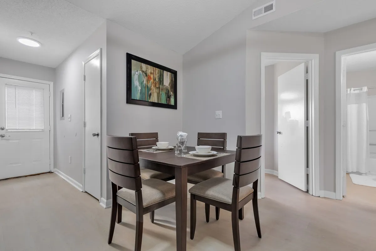 A view of a cozy dining area that also captures the entrance door and entry hall, with a dining table at the forefront and tasteful artwork on the wall. The scene highlights the welcoming transition space from the entry into the living areas.