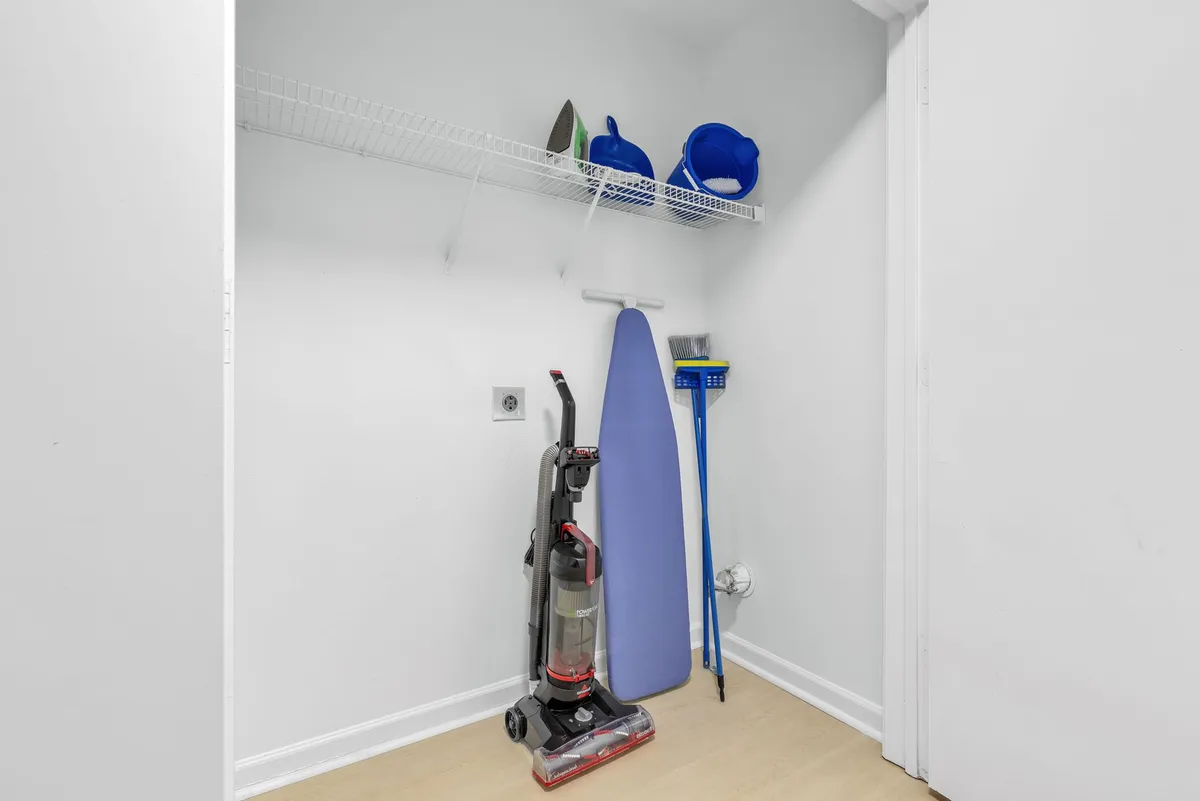 A practical interior space featuring a vacuum cleaner, ironing board, and cleaning supplies, clearly indicating a dedicated area for household chores and laundry. The room is tidy and well-organized, suggesting ease of upkeep and self-sufficiency during an extended stay.