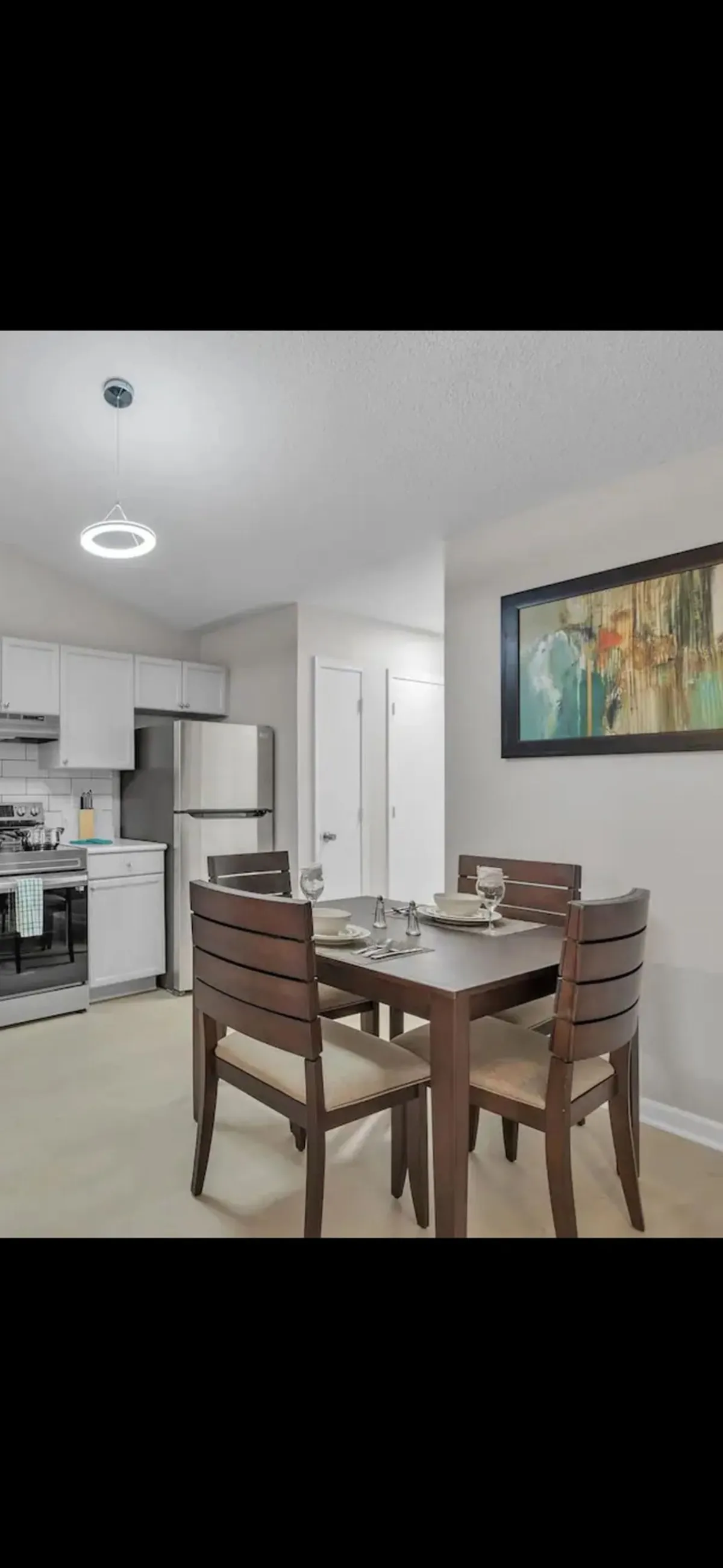 A view of the open dining area featuring a large dining table, contemporary chairs, and kitchen elements in the background. The artwork on the wall and natural light create a comfortable, modern vibe suited for meals, games, or planning activities.