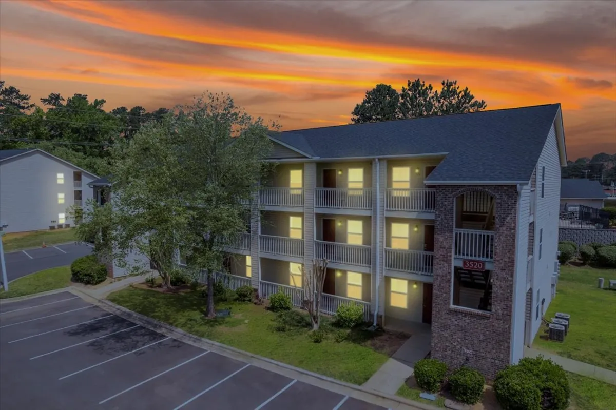 This exterior image captures the apartment building facade bathed in the warm glow of a vibrant sunset, with lush green foliage framing the scene. The balconies invite residents to relax and enjoy the evening ambiance, while the overall mood is one of welcome and peaceful community living.